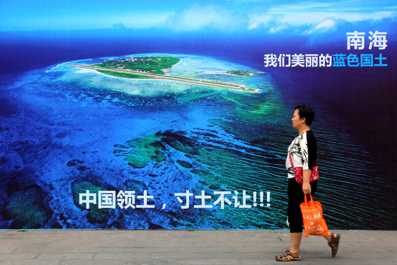 In this Thursday, July 14, 2016 photo, a woman walks past a billboard featuring an image of an island in South China Sea on display with Chinese words that read: "South China Sea, our beautiful motherland, we won't let go an inch" in Weifang in east China's Shandong province. China says if its interests in the South China Sea are threatened, it could declare an air defense identification zone in the area. Such a move would be seen as a threat to freedom of navigation, which the U.S. has promised to uphold. (Chinatopix via AP) CHINA OUT