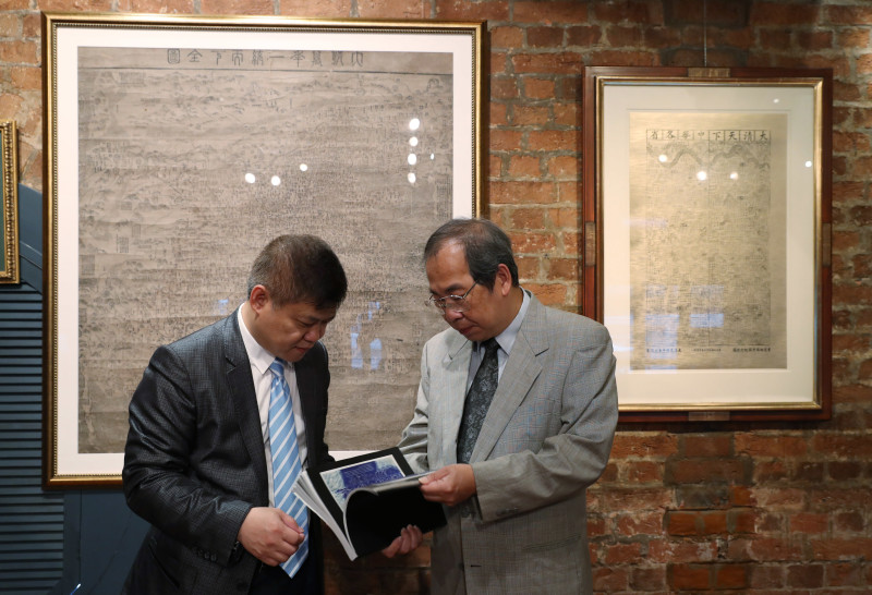 Sam Kwok, left, and Marcopolo Tam, members of a pro-China business group in Hong Kong, hold open a map in a book as they stand in front of two copies of larger maps dating from the Qing Dynasty purporting to back up China's claims to vast parts of the South China Sea, in Hong Kong, Thursday, July. 14, 2016. An international tribunal ruled in favor of the Philippines this week saying that China had no basis for expanses claims in the sea. (AP Photo/Kin Cheung)