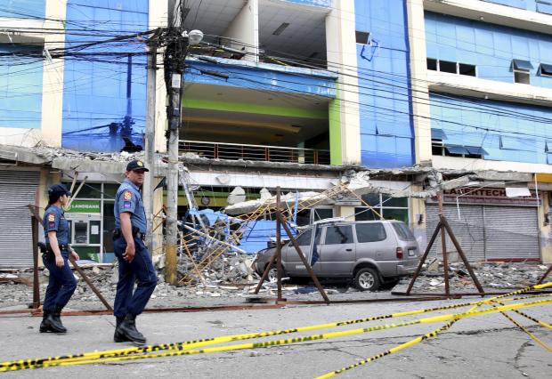 Police officers walk past a damaged building in Surigao City, two days after it was rocked by a powerful earthquake late Friday in Surigao del Norte province in Mindanao on Sunday, Feb.12, 2017. President Rodrigo Duterte has consoled survivors of the earthquake. (Photo by REY BANIQUET/Presidential Photographers Division, Malacañang Palace via AP)