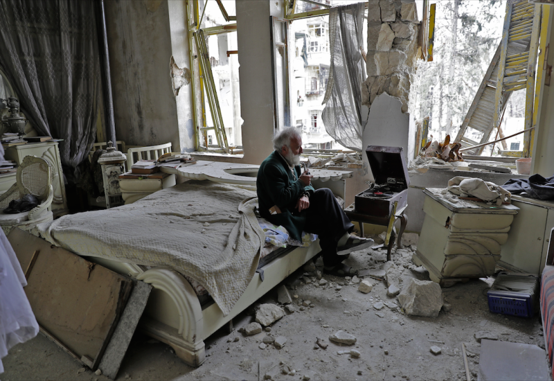 Mohammed Mohiedin Anis, or Abu Omar, 70, smokes his pipe as he sits in his destroyed bedroom listening to music on his vinyl player, gramophone, in Aleppo's formerly rebel-held al-Shaar neighbourhood.  JOSEPH EID / AFP